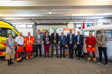 Group of medical and business professionals standing inside a garage between a yellow and a white ambulance