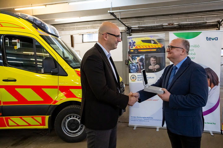 Two men shaking hands in front of a yellow ambulance