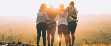 A group of friends hugging in front of a sunset