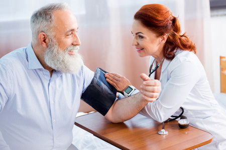 female doctor measuring pressure of smiling senior