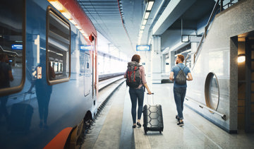 A couple carrying luggage heading to catch a train at the station.