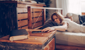 A woman in bed reaching for her phone