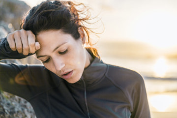 A woman leans her head on her hand, exhaling after an outdoor workout