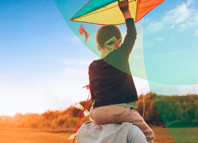 A boy on his parent's shoulder holding a kite